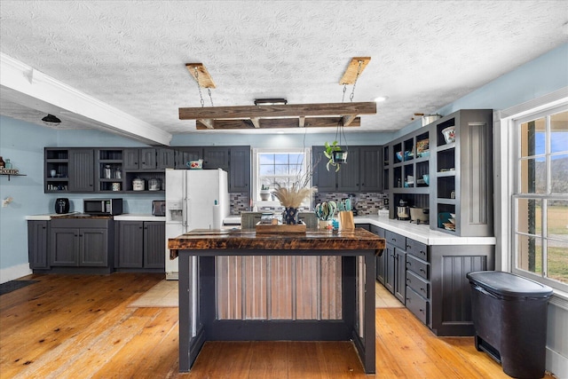 kitchen with light hardwood / wood-style floors, white fridge with ice dispenser, a textured ceiling, a kitchen island, and decorative backsplash