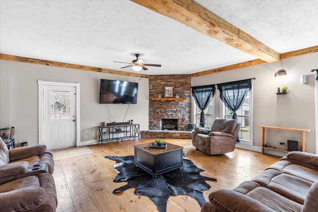 living room featuring beam ceiling, a stone fireplace, a textured ceiling, and light hardwood / wood-style flooring