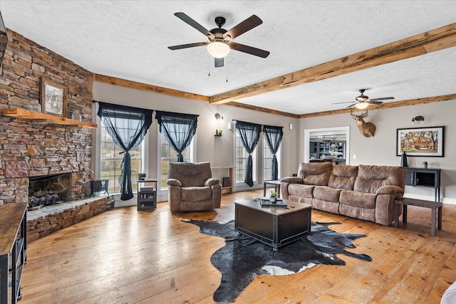 living room with beamed ceiling, a textured ceiling, a fireplace, and light wood-type flooring