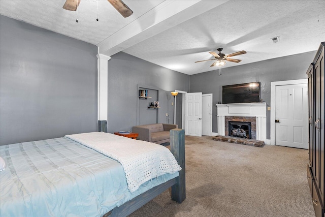 carpeted bedroom featuring ceiling fan, a stone fireplace, decorative columns, and a textured ceiling