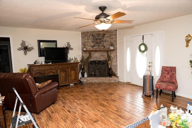 living room featuring hardwood / wood-style flooring, ceiling fan, a brick fireplace, and a textured ceiling