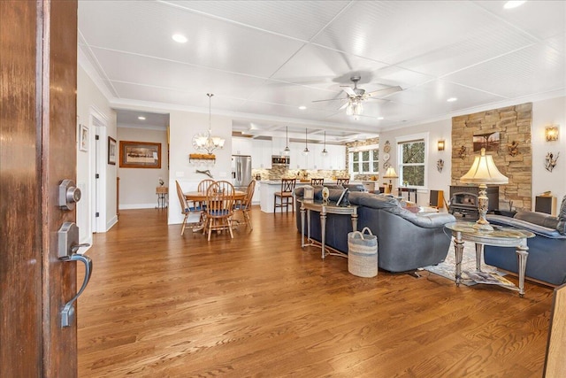 living room with ceiling fan with notable chandelier, baseboards, wood finished floors, and crown molding