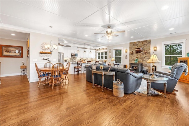 living room with ceiling fan with notable chandelier, crown molding, baseboards, and wood finished floors