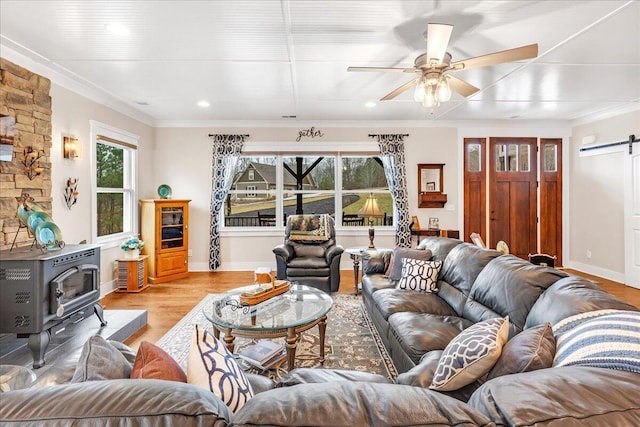 living area featuring a barn door, a ceiling fan, light wood-style floors, a wood stove, and crown molding