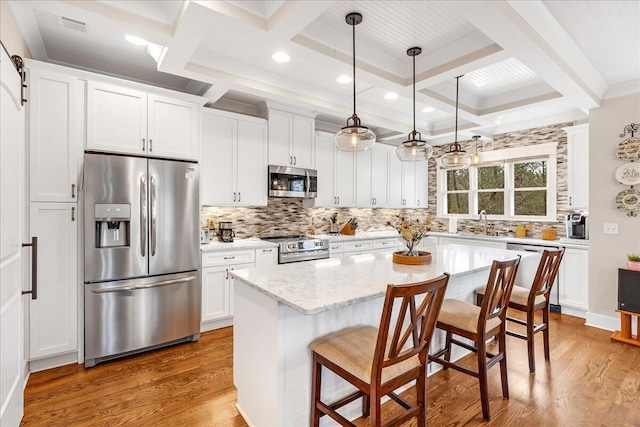 kitchen featuring a barn door, appliances with stainless steel finishes, white cabinets, a sink, and wood finished floors