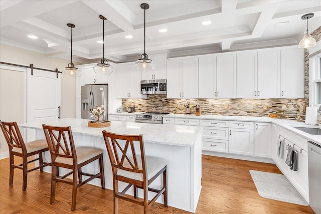 kitchen featuring a barn door, a kitchen island, stainless steel appliances, light wood-style floors, and backsplash