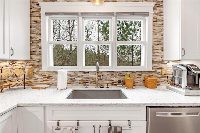 kitchen with stainless steel dishwasher, backsplash, a sink, and white cabinets