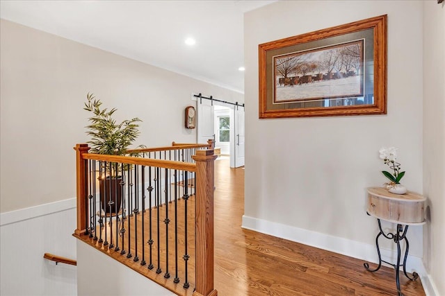 hall with a wainscoted wall, recessed lighting, a barn door, wood finished floors, and baseboards