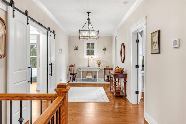 hall featuring a barn door, ornamental molding, wood finished floors, a chandelier, and baseboards