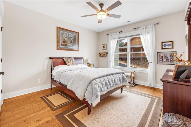 bedroom with a ceiling fan, visible vents, baseboards, and wood finished floors