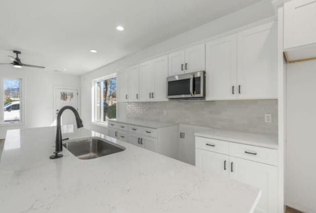 kitchen featuring tasteful backsplash, sink, white cabinets, ceiling fan, and light stone countertops