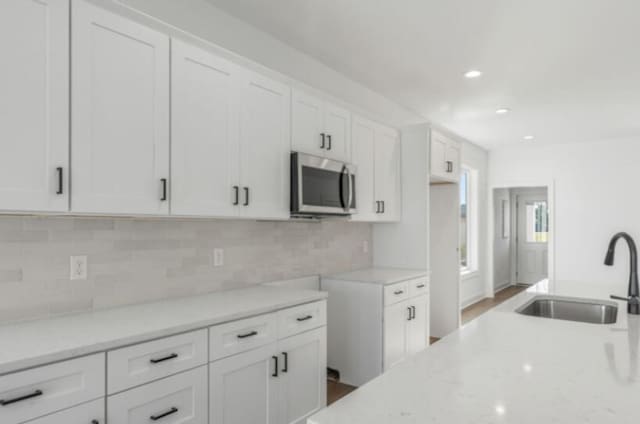 kitchen featuring light stone counters, sink, tasteful backsplash, and white cabinets