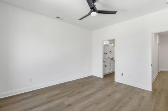 unfurnished bedroom with ceiling fan, ensuite bath, and wood-type flooring