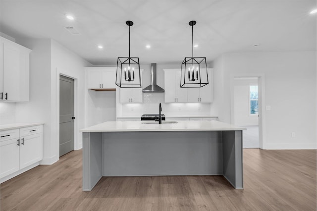 kitchen featuring pendant lighting, white cabinetry, an island with sink, sink, and wall chimney range hood