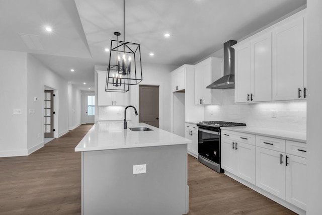 kitchen featuring sink, gas range, wall chimney range hood, a kitchen island with sink, and white cabinets