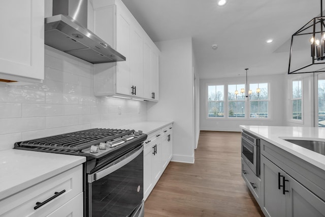 kitchen with white cabinetry, a chandelier, hanging light fixtures, stainless steel appliances, and wall chimney exhaust hood