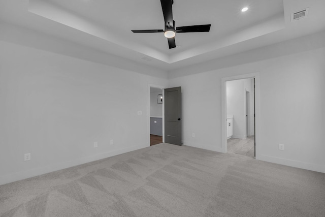 unfurnished bedroom featuring connected bathroom, light colored carpet, ceiling fan, and a tray ceiling