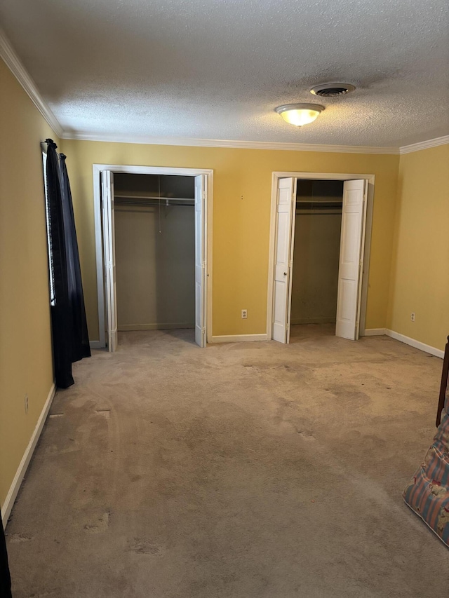 unfurnished bedroom featuring light carpet, a textured ceiling, ornamental molding, and multiple closets