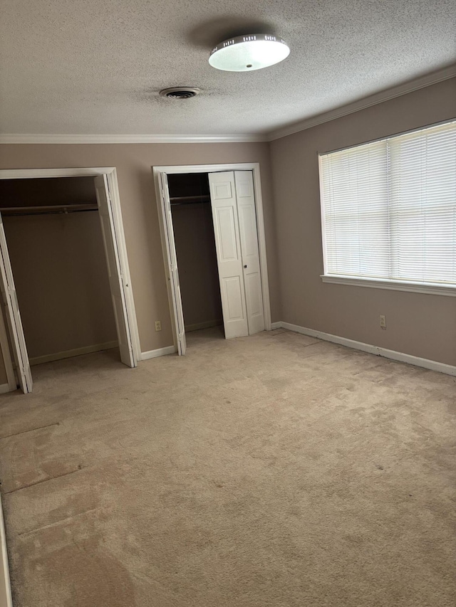 unfurnished bedroom with light colored carpet, ornamental molding, a textured ceiling, and two closets