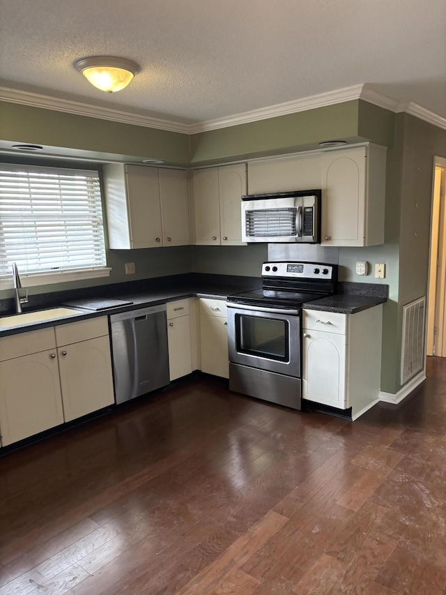 kitchen with appliances with stainless steel finishes, sink, dark hardwood / wood-style flooring, ornamental molding, and a textured ceiling