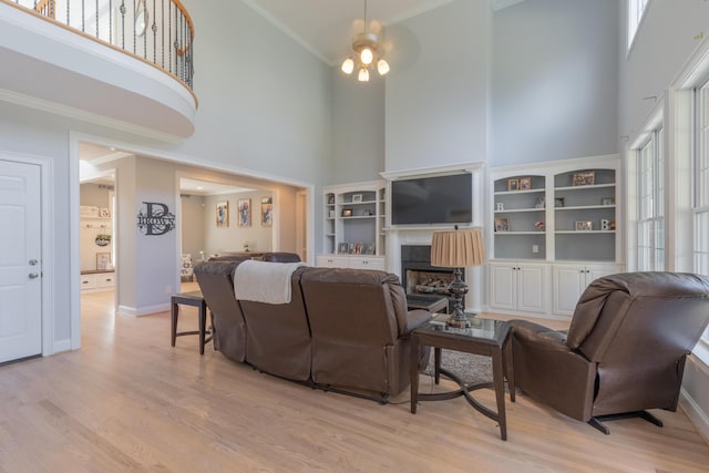 living room featuring a high ceiling, ornamental molding, a fireplace, and light hardwood / wood-style flooring