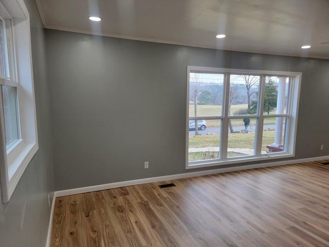 empty room featuring visible vents, baseboards, ornamental molding, and wood finished floors