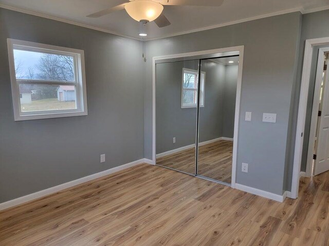 unfurnished bedroom featuring crown molding, ceiling fan, light wood-type flooring, a closet, and baseboards