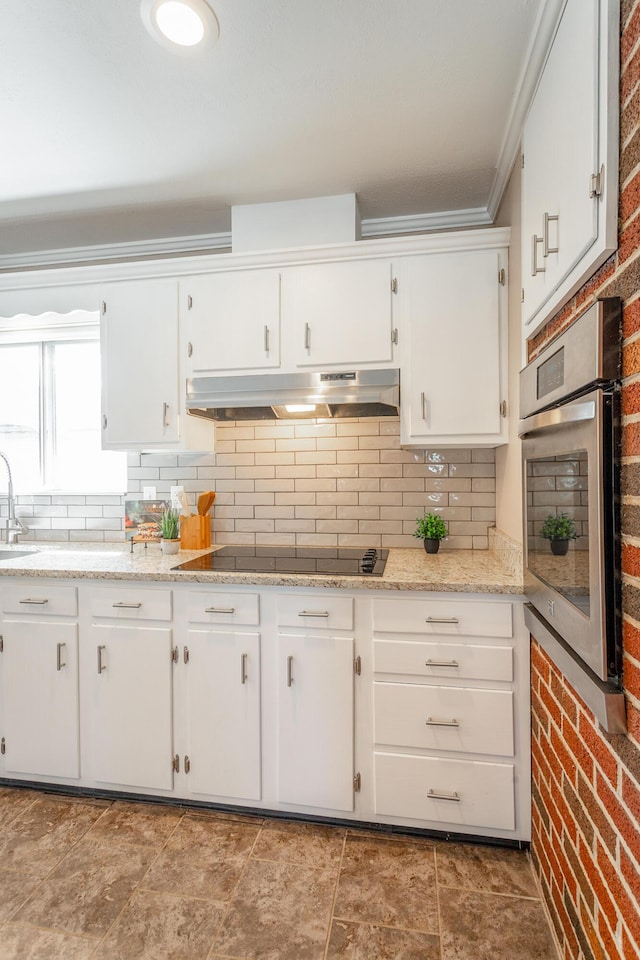 kitchen featuring tasteful backsplash, brick wall, stainless steel oven, and white cabinets