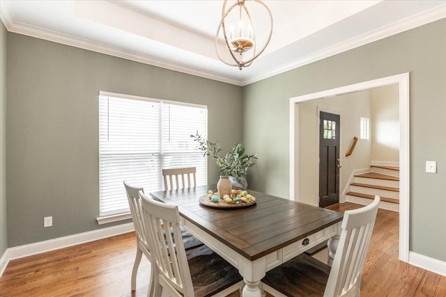 dining area with a tray ceiling, crown molding, light wood-style flooring, and baseboards