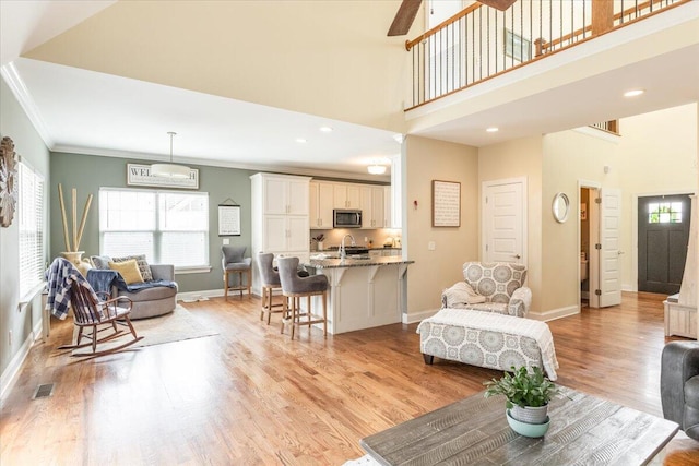 living room with a towering ceiling, baseboards, visible vents, light wood-style floors, and crown molding