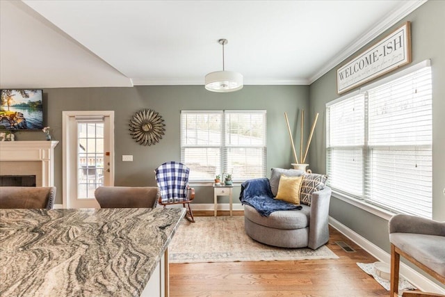 living area featuring a fireplace, wood finished floors, visible vents, baseboards, and crown molding