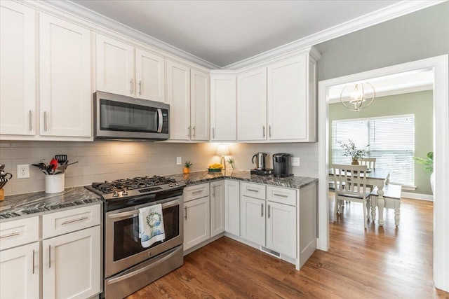 kitchen featuring decorative backsplash, dark stone counters, appliances with stainless steel finishes, wood finished floors, and white cabinetry