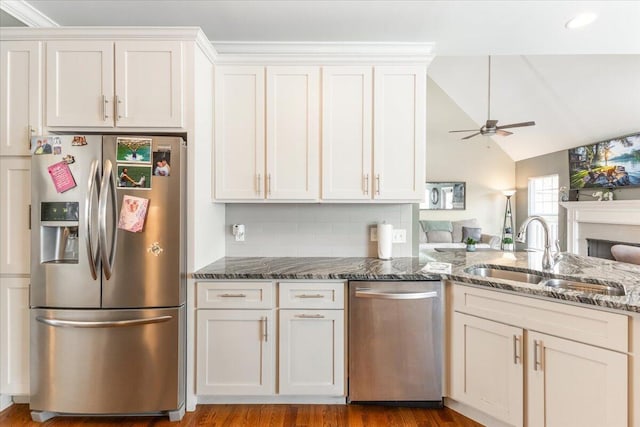 kitchen with dark stone counters, lofted ceiling, open floor plan, stainless steel appliances, and a sink