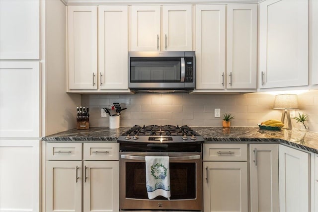 kitchen featuring dark stone counters, stainless steel appliances, white cabinetry, and decorative backsplash