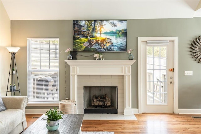 living room featuring a brick fireplace, wood finished floors, visible vents, and baseboards