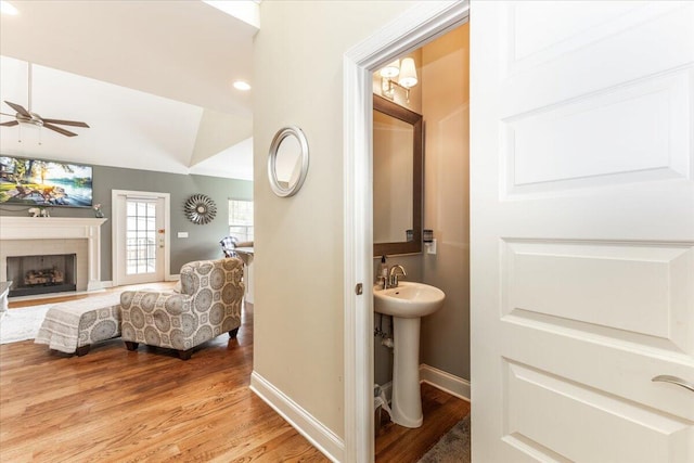 bathroom featuring baseboards, a ceiling fan, lofted ceiling, wood finished floors, and a brick fireplace