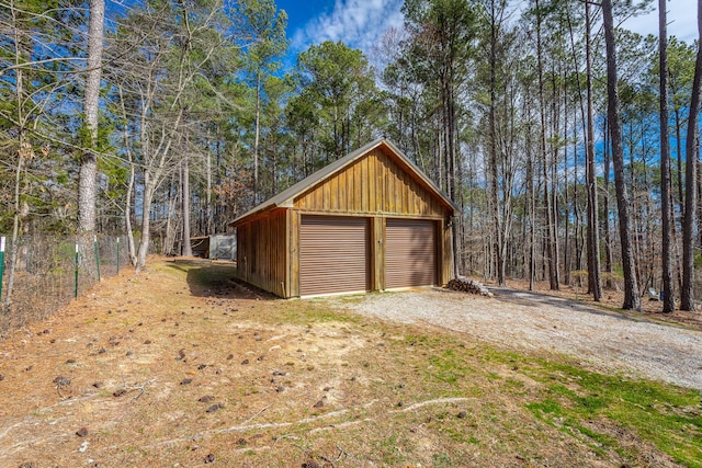 detached garage featuring fence and a view of trees