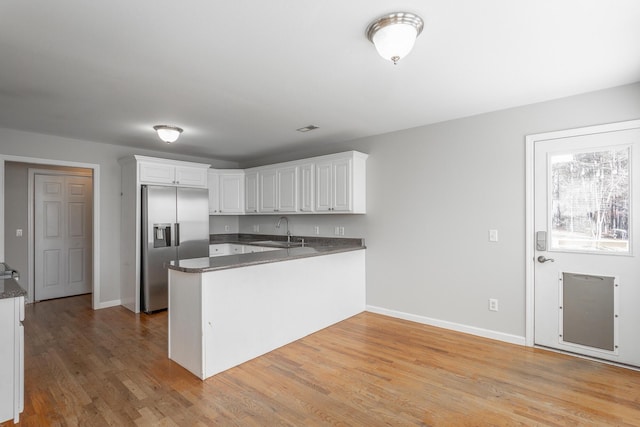 kitchen with a peninsula, white cabinets, stainless steel fridge with ice dispenser, and a sink