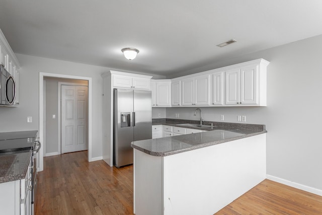 kitchen featuring visible vents, a sink, wood finished floors, appliances with stainless steel finishes, and a peninsula