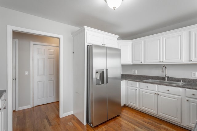 kitchen with dark countertops, wood finished floors, stainless steel fridge, white cabinetry, and a sink