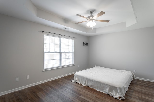 bedroom with visible vents, baseboards, a tray ceiling, and dark wood-style flooring