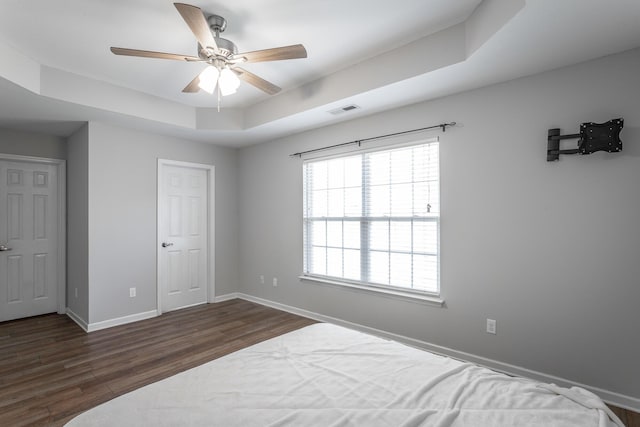 bedroom featuring a ceiling fan, baseboards, visible vents, dark wood finished floors, and a tray ceiling