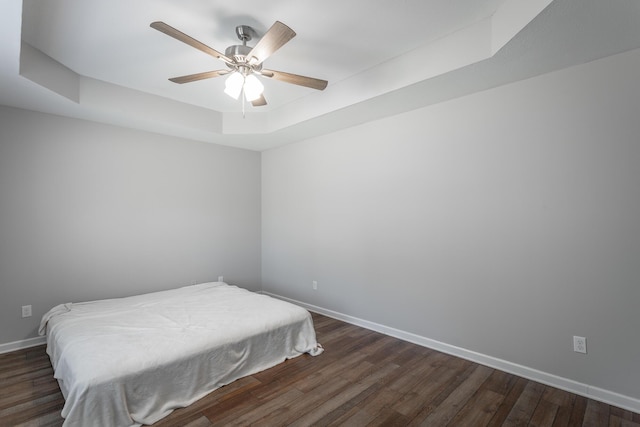 bedroom with a tray ceiling, baseboards, ceiling fan, and dark wood-style flooring