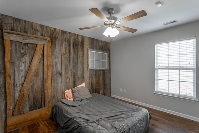 bedroom featuring visible vents, wood finished floors, baseboards, and wood walls