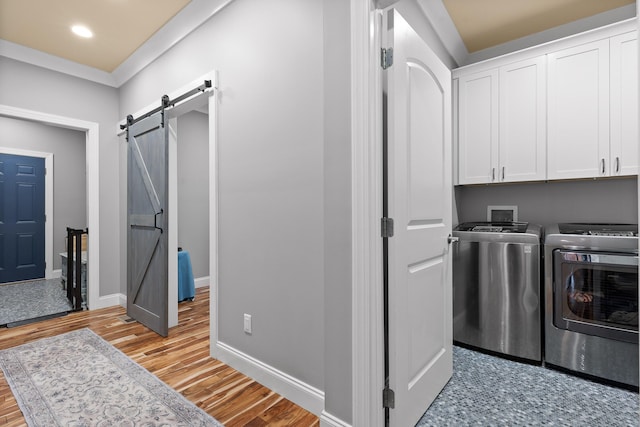 clothes washing area featuring cabinets, ornamental molding, light hardwood / wood-style floors, a barn door, and washer and clothes dryer