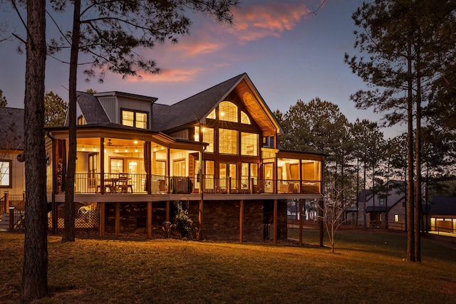 back house at dusk featuring a sunroom, a deck, and ceiling fan