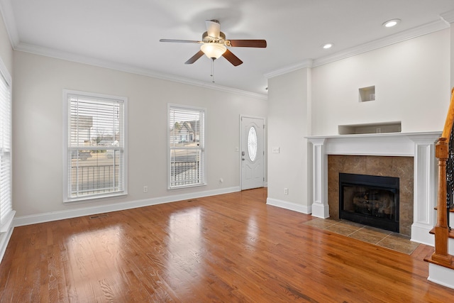 unfurnished living room featuring a tiled fireplace, wood-type flooring, ceiling fan, and crown molding