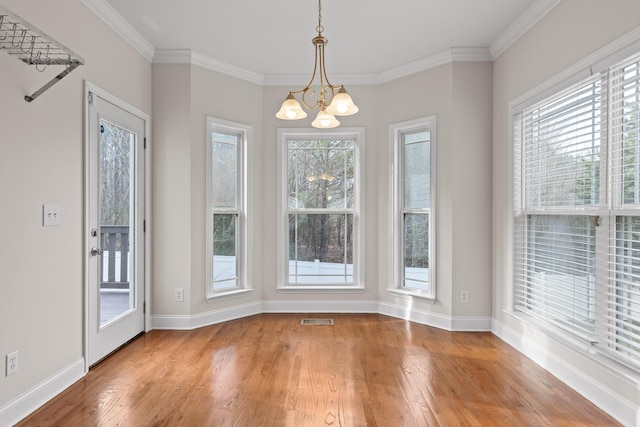 unfurnished dining area featuring crown molding, hardwood / wood-style flooring, and a chandelier