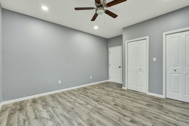 unfurnished bedroom with ceiling fan, light hardwood / wood-style floors, and multiple closets