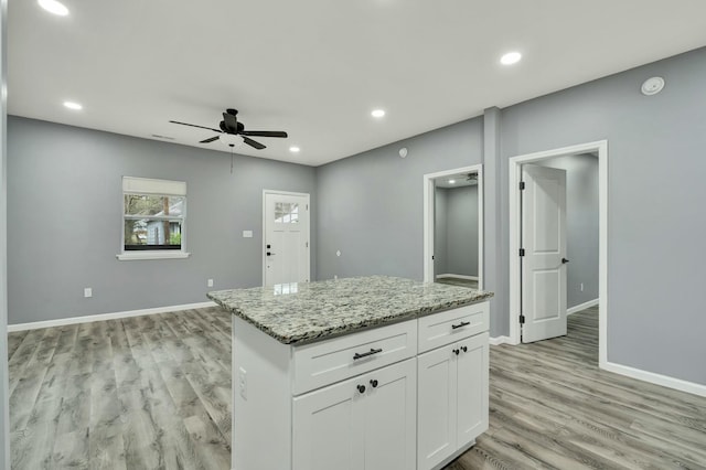 kitchen featuring light hardwood / wood-style flooring, ceiling fan, light stone countertops, white cabinets, and a kitchen island